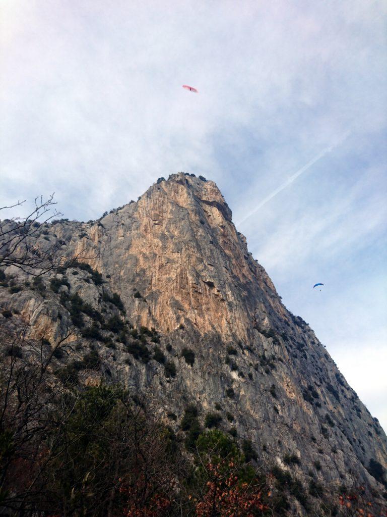 La fantastica parete verticale del Piccolo Dain visto dal sentiero di discesa, con tanto di parapendii svolazzanti