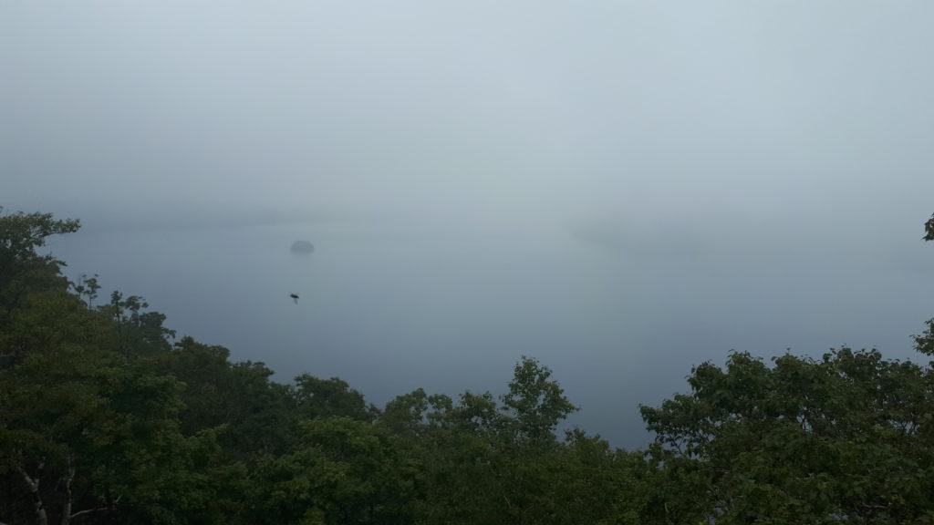 il lago di Mashu coperto dal vapore e dalle nubi: si intravede l'isoletta al suo centro