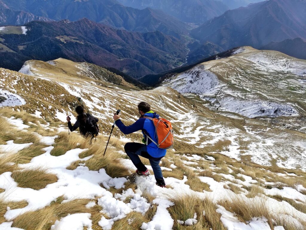 Dalla cima del Triomen ci si abbassa su erba e neve spostandosi prima verso est, per poi scendere a valle quando si raggiunge un ometto