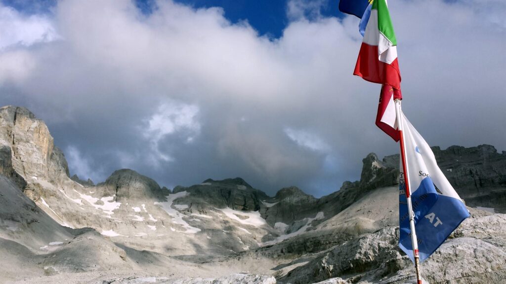 Le colorate bandiere del rifugio al contrasto con l'anfiteatro di cime che svettano attorno all'(ex) ghiacciaio d'Agola, orma ridotto all'osso, ma con ancora un paesaggio da urlo
